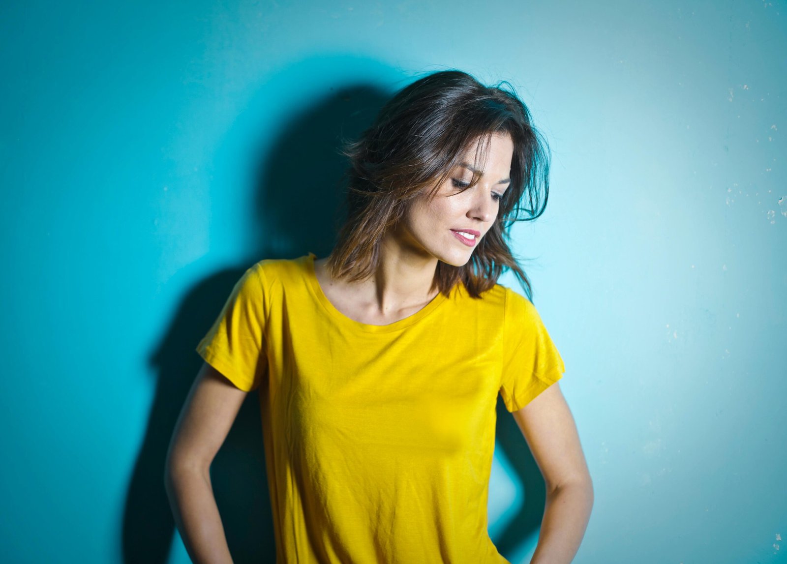 Portrait of a smiling woman in a yellow shirt against a blue wall.